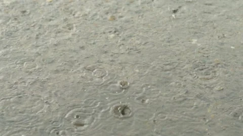 Heavy rain drops falling on a large puddle on concrete ground Stock Footage 338365264