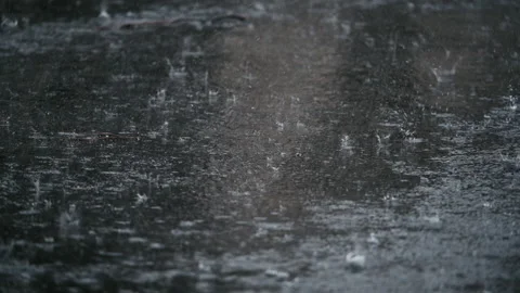 Heavy rain falling on asphalt road with visible splashes and water ripples. Slow Vídeo Stock 332185242