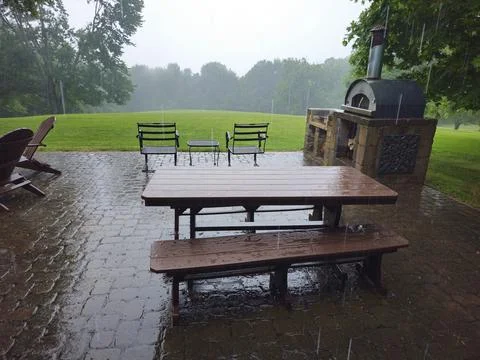 Heavy rain falling on picnic table on patio with pizza oven in background Stock Photos