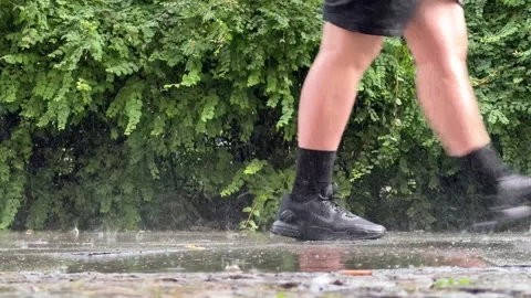 Heavy rain falling in puddles on sidewalk with of a pedestrian walking by Stock Footage 277340091