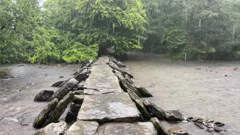 Heavy rain falling onto a stone bridge over a river Stock Footage 262661861