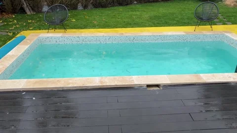 Heavy rain falling on the turquoise water of a modern swimming pool in a Stock Footage 319483906