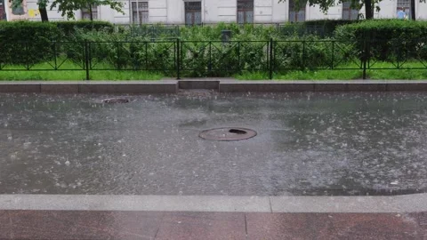 Heavy rain falling on urban canal with sewer grate, verdant hedge backdrop Vídeo Stock 345700314