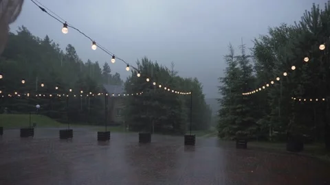 Heavy rain falls in yard of the house, decorated with garlands of light bulbs. Stock Footage 181880863