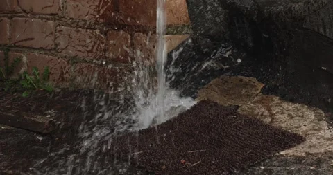 Heavy rain flowing from a buildings gutter downspout, splashing onto the wet Stock Footage 334574193