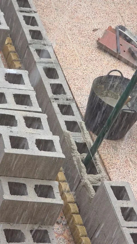 Heavy rain halting concrete block wall construction with tools and raw cemen Stock Footage 346103866