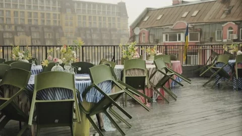 Heavy rain on the terrace of a cafe. Empty wet tables decorated with flowers on Stock Footage 318066012