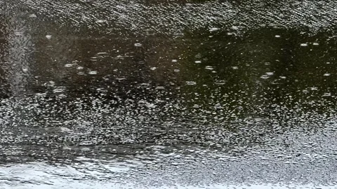 Heavy rainfall hitting wet asphalt road surface on empty urban street Stock Footage 312382228