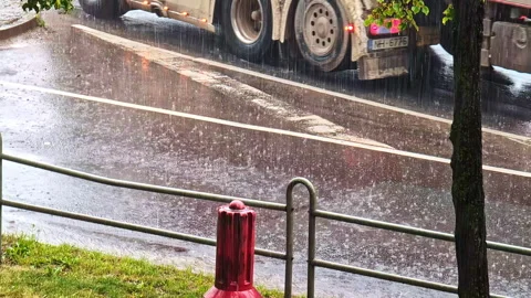 Heavy rainfall pours onto a busy roadside as cars drive through sheets of Stock-Footage 325057478