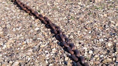 Heavy rusted anchor chain lying on a gravel and pebble shore Vidéo 343574548