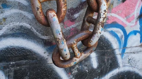A heavy rusty anchor chain sways slowly against a concrete wall with graffiti. Stock Footage 247853197