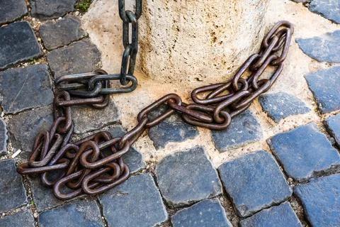 Heavy rusty metal chain lying on cobblestone pavement Stock Photos