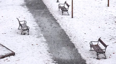 Heavy snow falling over benches in city park while wind blows dry leaves Stock Footage 67489308