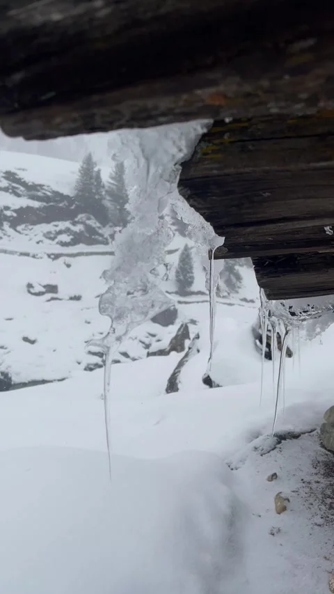 Heavy Snowfall Behind Frozen Icicles with Distant Winding Mountain River Video stock 327690450