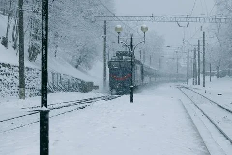 Heavy snowfall covers the railway tracks and surrounding trees as a locomotiv Stock Photos
