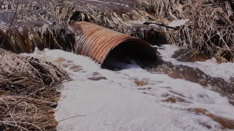 Heavy spring runoff pouring from a rusty culvert and running over a road Video stock 129880878