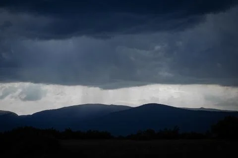 Heavy Storm Clouds and Rainfall Curtain Above Distant Mountain Ridges Stock-Fotos