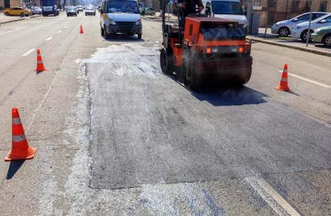 Heavy vibratory road roller compacts asphalt on the repaired part of the city Stock Photos
