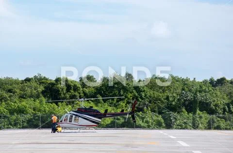 The helicopter is being prepared for take-off, stands on a helipad with a b.. Stock Photos