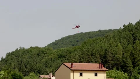 A helicopter drops water on a developing forest fire near buildings. Rocca di Stock Footage 341133557