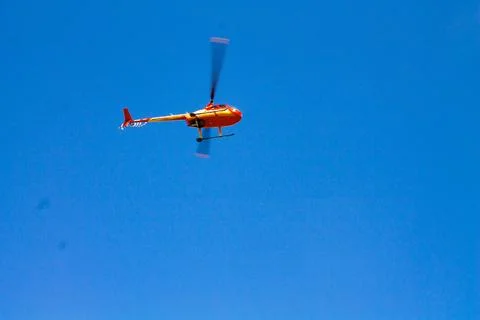 The helicopter flies against the background of a cloudless blue sky. Stock Photos