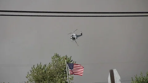 Helicopter flies over American flag towards smokey fire Stock Footage 114415575