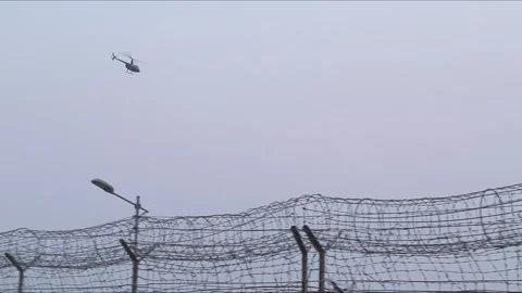 A helicopter flies over a barbed wire fence . Stock Footage 266566185