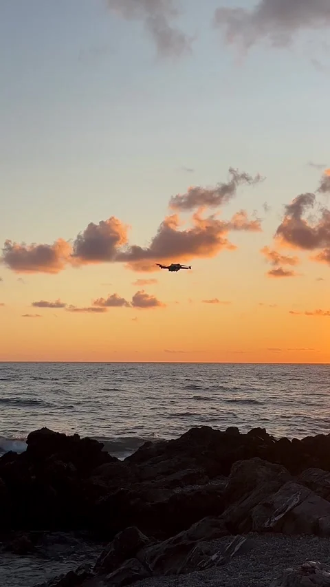 Helicopter Flies Over Ocean During Sunset Near Rocky Shoreline Stock Footage 318387093