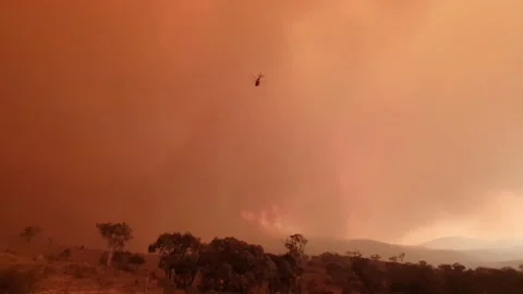 A Helicopter Flies Towards a Bushfire Through Smoky Orange Clouds Stock Footage 195281246
