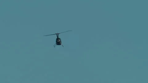 Helicopter flying high in a vast blue sky, illustrating themes of air travel, Stock Footage 339797917