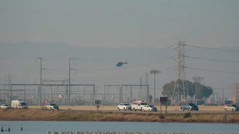 A helicopter hovering low near a complex of high-voltage power lines Stock Footage 328694776