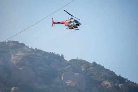 A helicopter from the LAFD performs a water drop on burning brush near firefi 写真素材