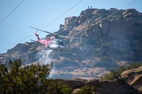 A helicopter from the LAFD performs a water drop near firefighters at a brush Stock Photos