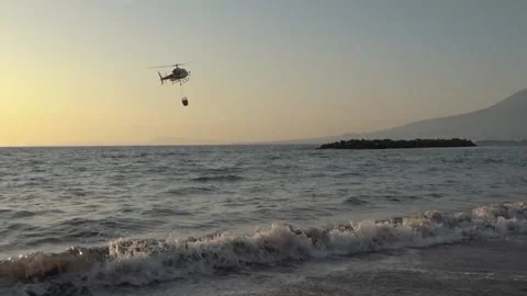A Helicopter Refills The Bucket At The Beach During A Fire Fighting Operation Video stock 140198191