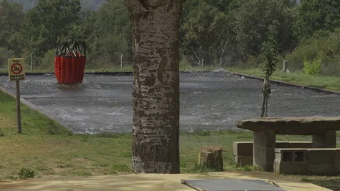 Helicopter skillfully lifting a full Bambi bucket from pool in slow motion Stock Footage 318281192
