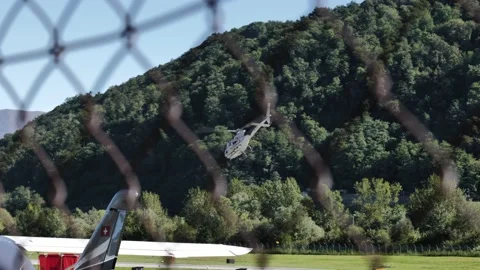 Helicopter Taking Off and Flying over Lugano Airport Against Sky with Mountain Stock Footage 211403079