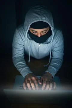 Hell crack that code. High angle shot of a man in a hoodie and mask hacking a Foto stock