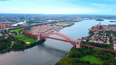 Hell Gate Bridge spans the East River beside New York parkland. A red steel arch Stock Footage 347899162