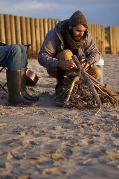 Hell get it started. A young man building a fire on the beach. Stock Photos