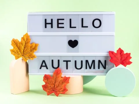 Hello autumn text on lightbox with fall leaves on green and orange podiums Stock Photos