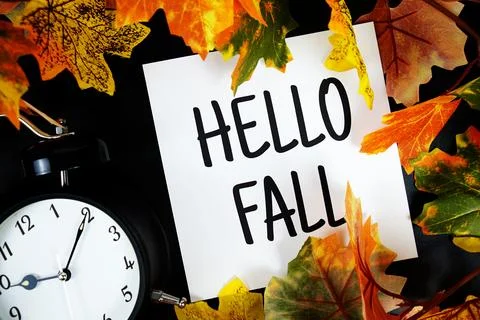 Hello Fall text with alarm clock and maple leaf decoration on wooden backgrou Stock Photos