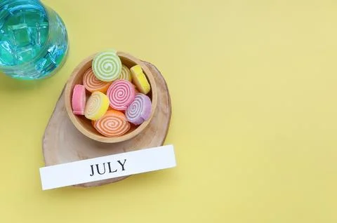 Hello July, July text on white wood block and jelly sweet on yellow background.  Stock Photos