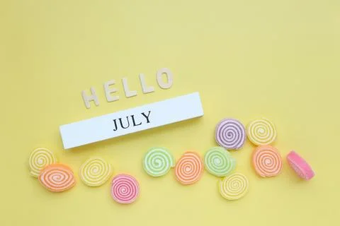 Hello July, July text on white wood block and jelly sweet on yellow background.  Stock Photos
