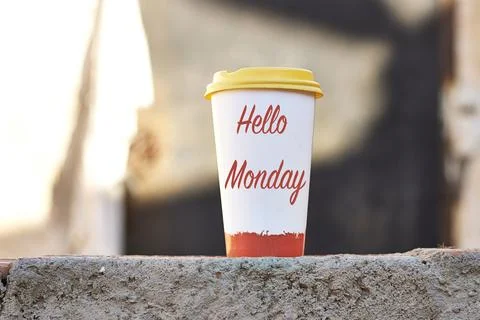 Hello Monday Coffee Cup With Yellow Lid On Concrete Wall In Morning Light Stock Photos