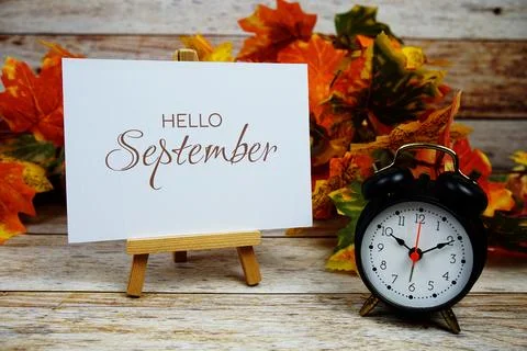 Hello September text with alarm clock and maple leaf decoration on wooden b.. Stock Photos