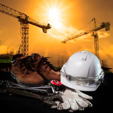 Helmet and construction equipment with building and crane against dusky sky Stock Photos