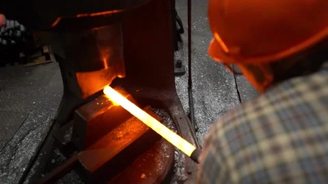 A helmeted blacksmith was forging a piece of hot metal under a mechanical hammer Video stock 143320379