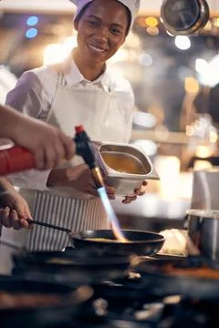 Helper looking chef while burning a meal with flame torch. Cook in Professi.. Stock Photos