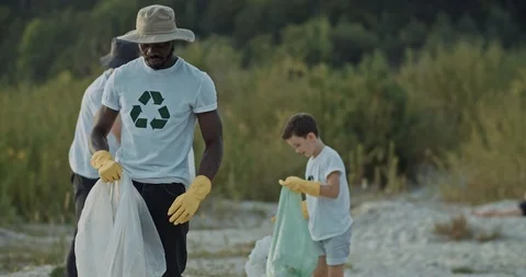 Helpful african guy picking up plastic garbage on sandy beach cleaning down the Stock Footage 115384610