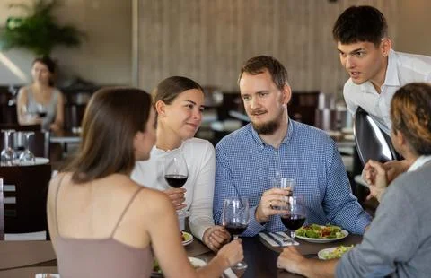 Helpful young waiter taking order from two couples in restaurant Stock Photos